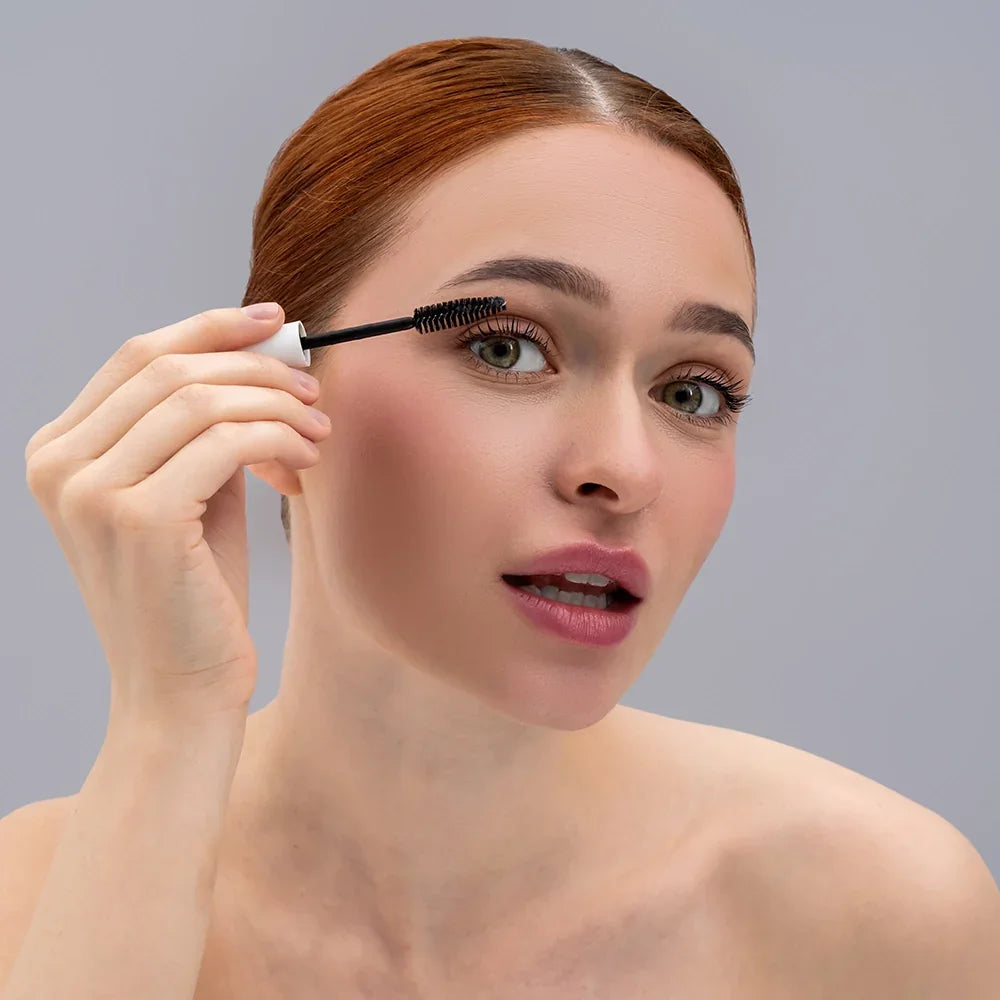 Vrouw met rood haar gebruikt mascara voor langere wimpers - Cryon Schoonheidssalon